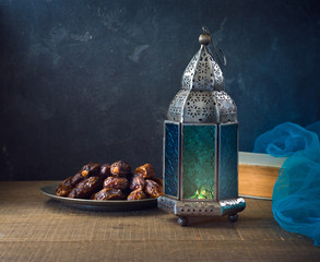 Lightened lantern and dates fruit on wooden table over dark background. Ramadan kareem holiday...