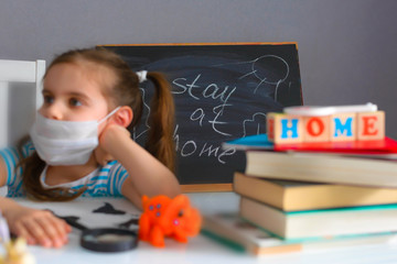 Stay at home. Quarantine. Covid-19. Distance learning online education. School girl in a medical mask is studying at home with a laptop in her hand and doing school homework.