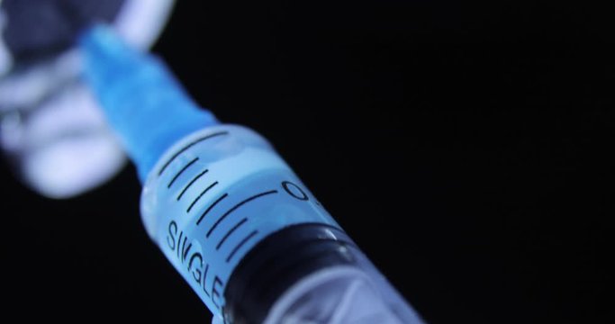 Dials blue medicament coronavirus vaccine into syringe on black background during pandemic. Coronavirus vaccination concept, COVID-19. Needle and blue vaccine bottle at hospital. Epidemic concept.