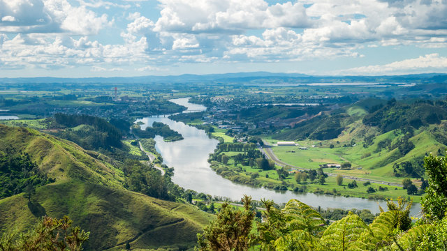 Panoramic view on river valley with lush green and river flowing through the shot during sunny day with blue sky and some clouds. On the picture is Waikato, longest river in New Zealand.