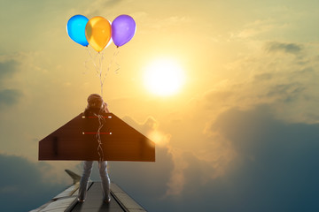 Cute little girl wear diy winged and captain's hat use binocular looking at sun imagine that four balloons can make her fly stand on airplane's wing
