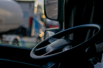 Truck cabin with the steering wheel in the foreground and trucks in the background