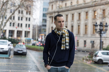 Young Man with Earphones and Head Turned in Urban Setting