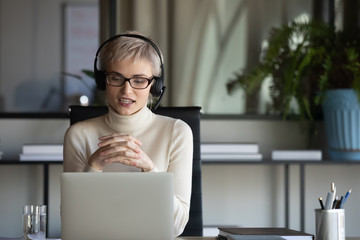 Focused pleasant 30s businesswoman in eyeglasses wearing wireless headphones with microphone,...