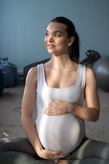 Fototapeta na wymiar A pregnant girl sits in a lotus position and holds on to her stomach. A woman is doing yoga in the 3rd trimester. A bubbling mom is waiting.