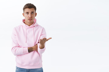 Why you being mean to me. Portrait of concerned and frustrated blond man asking question, cant understand what wrong, pointing palm at camera and looking confused, white background