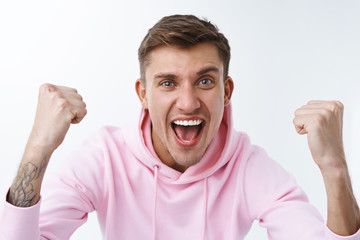 Close-up portrait of cheerful supportive young blond man, sport team fan cheering and chanting during competition, watching match online, raise hands up triumphing, winning, celebrate scored goal