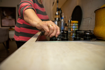 The senior woman's touching hand switches on the hotplate because she wants to cook something. She's in her kitchen.