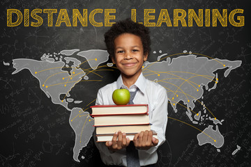 Distance learning and back to school concept. Smiling black child boy against World map on blackboard background