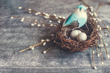 Easter background. Nest with easter eggs and decorative blue bird on wooden background. Selective focus.