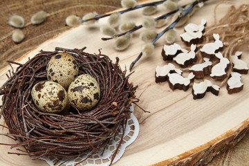 Quail eggs in a nest, wooden hares and pussy-willow branches with buds on a wooden board. Easter concept