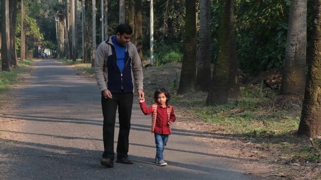 An Indian brunette father and his baby boy in winter garments walking in a forest path in winter afternoon in natural green background. Indian lifestyle and parenthood.