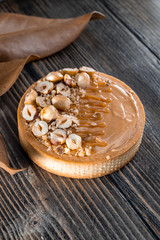 Delicious tart with caramel and halved hazelnuts  on the wooden background. Beautiful dry leaves near. Day light, natural color grade