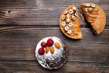 Two delicious tarts, one with caramel and hazelnuts and another with dark chocolate, raspberries, almond and powdered sugar on the wooden background. Top view, flat lay, natural light