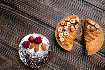 Two delicious tarts, one with caramel and hazelnuts and another with dark chocolate, raspberries, almond and powdered sugar on the wooden background. Top view, flat lay, natural light