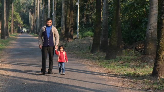 An Indian brunette father and his baby boy in winter garments walking in a forest path in winter afternoon in natural green background. Indian lifestyle and parenthood.