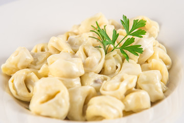 Dish of tortellini stuffed with meat and cream and a sprig of parsley.