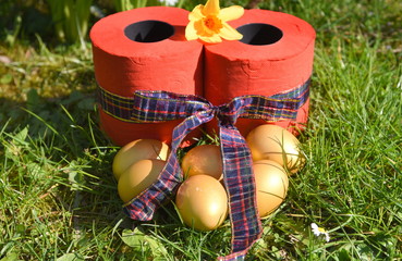 Osternest mit goldenen Eiern und roten Klopapierrollen mit Schleife auf einer grünen Wiese