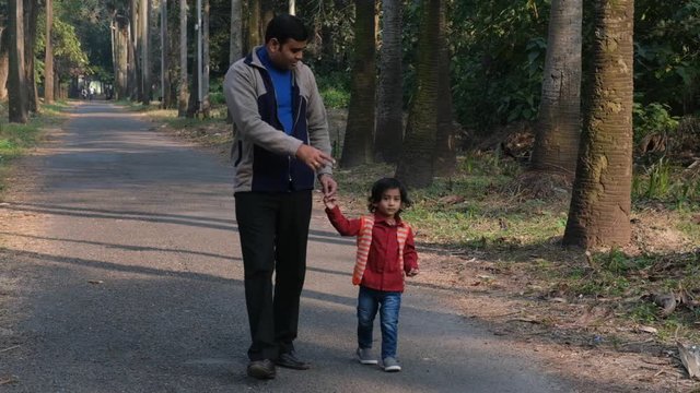 An Indian brunette father and his baby boy in winter garments walking in a forest path in winter afternoon in natural green background. Indian lifestyle and parenthood.
