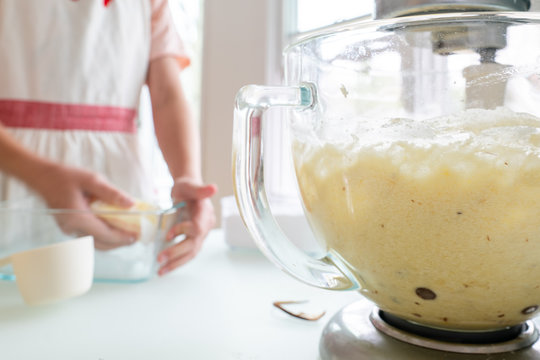 Closeup of a kitchen mixer with child's hands greasing pan in the background