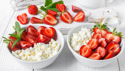 White bowl with fresh red ripe strawberries and natural cottage cheese