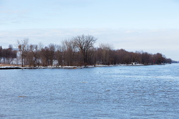 Pretty St. Lawrence River cove, farm and scattering of houses seen through bare branches during an early spring morning, Lotbinière, Quebec, Canada