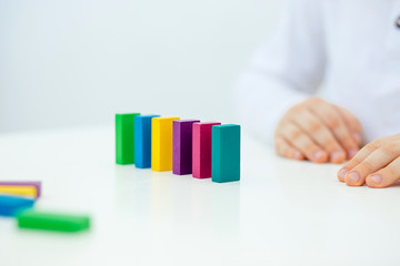 Building items in a single row. Concept of diagnostics of children's autism. A child plays with a colored wooden construction tool. Close.
