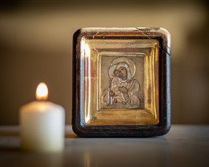 A candle burning in front of an icon of holy mother and child