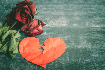 Divorce concept - red broken heart with old rose on wooden background.