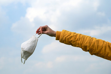 Woman is holding the textile home made face mask used for protection against viruses while walking in the nature. Symbol for protest against regulations or freedom after end of pandemic. 
