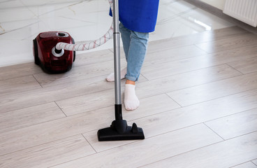 The girl in light jeans is vacuuming the floor.