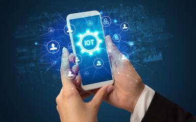 Female hand holding smartphone with IOT abbreviation, modern technology concept