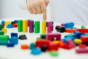 Building items in a single row. Concept of diagnostics of children's autism. A child plays with a colored wooden construction tool.