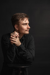 portrait of a man in a black shirt on a black background. He turned away. Hands clasped together