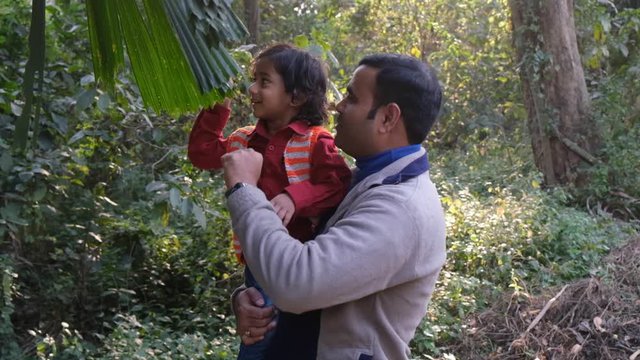 An Indian brunette father and his baby boy in winter garments enjoying themselves in winter afternoon on a  dry grass field in forest background. Indian lifestyle and parenthood.