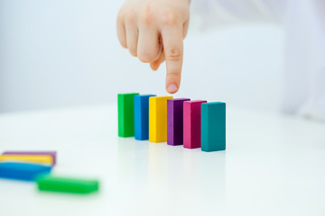 Building items in a single row. Concept of diagnostics of children's autism. A child plays with a colored wooden construction tool. Close.
