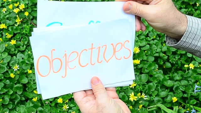 Man presents definition of goals concept as godly objectives assure lasting success by using handwritten cardboard sheets on a garden background