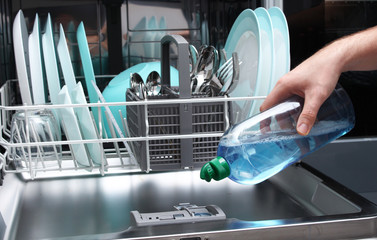 Loading the gloss liquid into the dishwasher. Man filling dishwasher with gloss liquid.