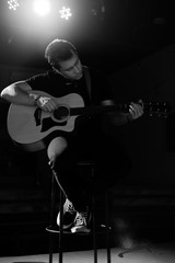 A young handsome guy of European appearance plays an acoustic guitar and sits on a chair. Black and white photography.