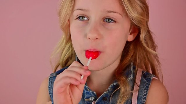 Close-up charming angelic beautiful girl licks a red candy, slow motion