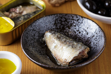 Lata de Sardinha em conserva aberta, pão azeite e azeitonas sobre mesa de madeira