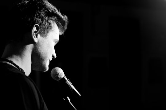 Young handsome guy emotionally sings and speaks into the microphone. Black and white photography