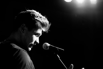 Young handsome guy emotionally sings and speaks into the microphone. Black and white photography