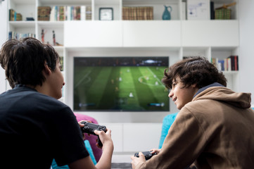 Two boys sitting at home playing video games on game console