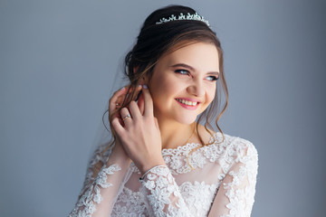 the bride in the wedding dress fixes the earring on the wall bac