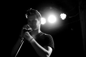 Young handsome guy emotionally sings and speaks into the microphone. Black and white photography