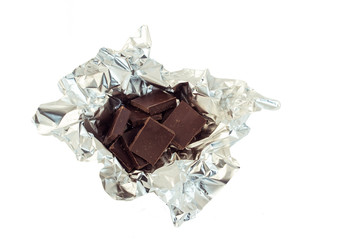 a mountain of squares of dark chocolate lies on the crumpled foil
