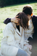 Fototapeta premium Loving hipster couple walking in the field, kissing and holding hands, hugging, lying in the grass in the spring at sunset. Photo with lens flare