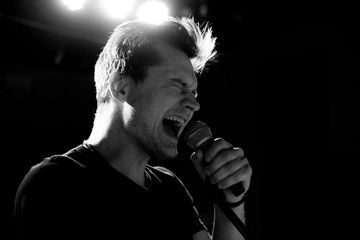Young handsome guy emotionally sings and speaks into the microphone. Black and white photography