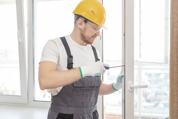 Worker man installs plastic windows white lock and seal adjustment
